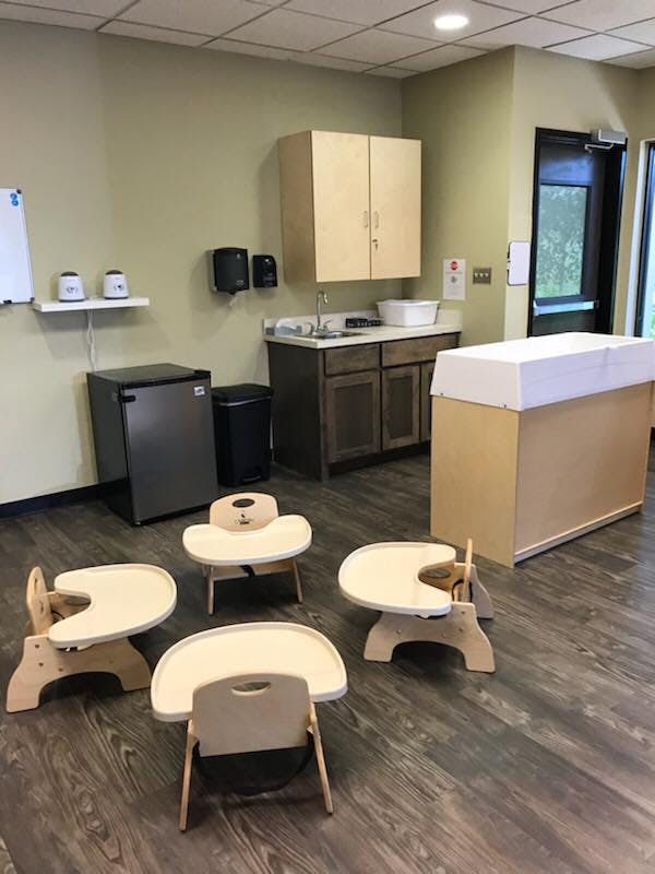 Four small wooden chairs with attached trays in a room with a sink and changing table
