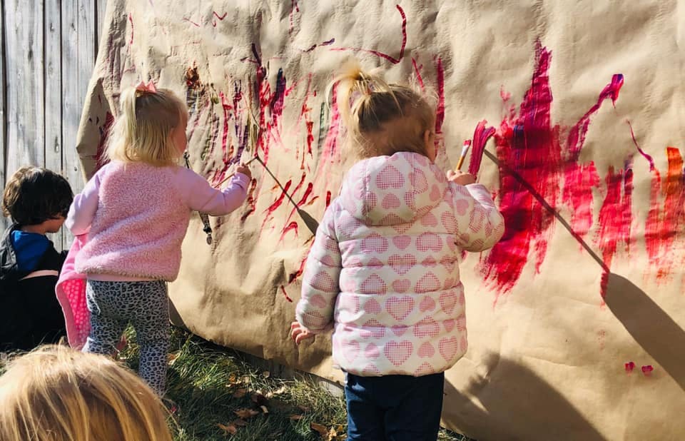 Children painting on a large sheet of paper outdoors