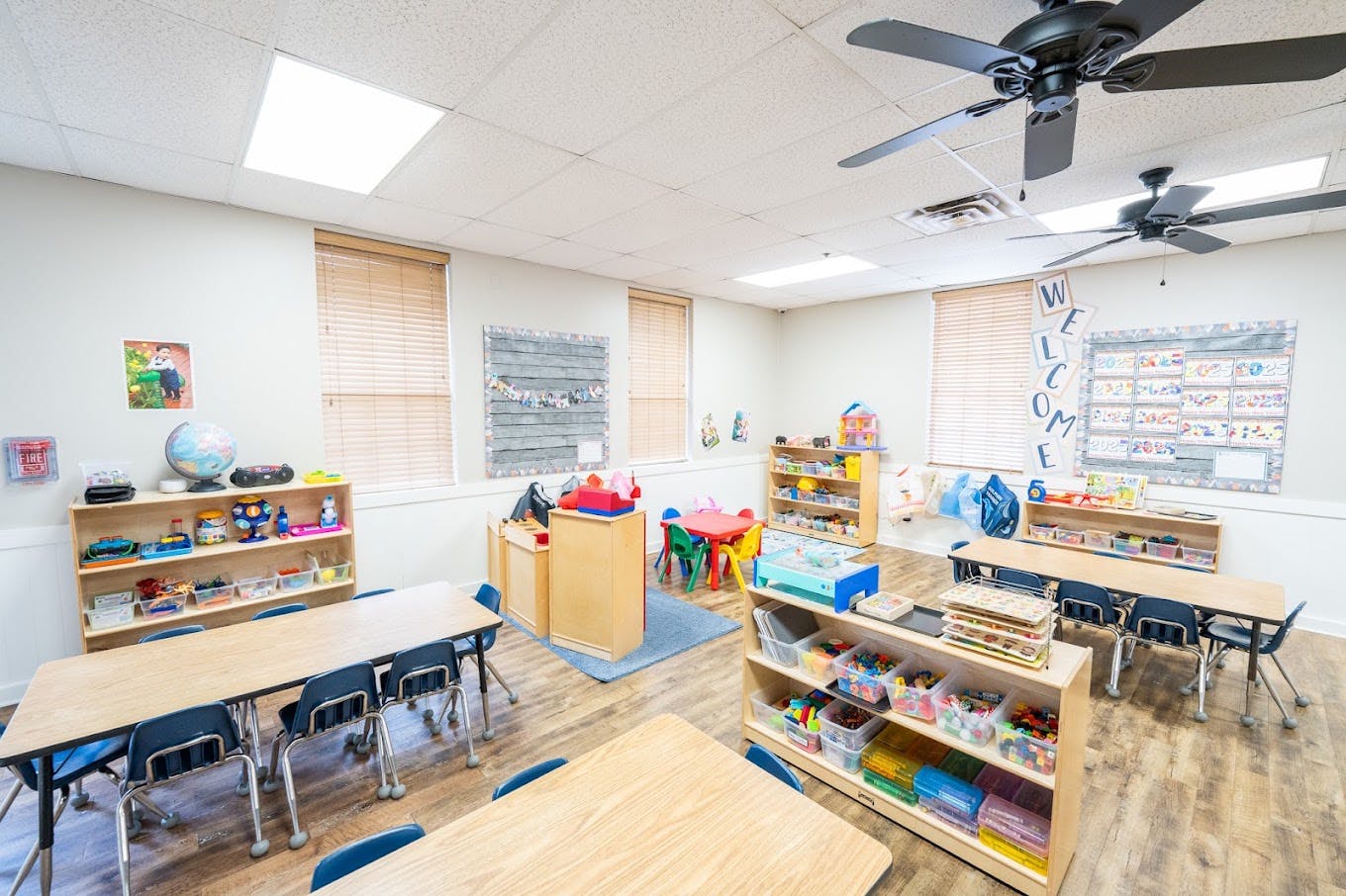 Classroom interior with small tables, chairs, and shelves full of toys