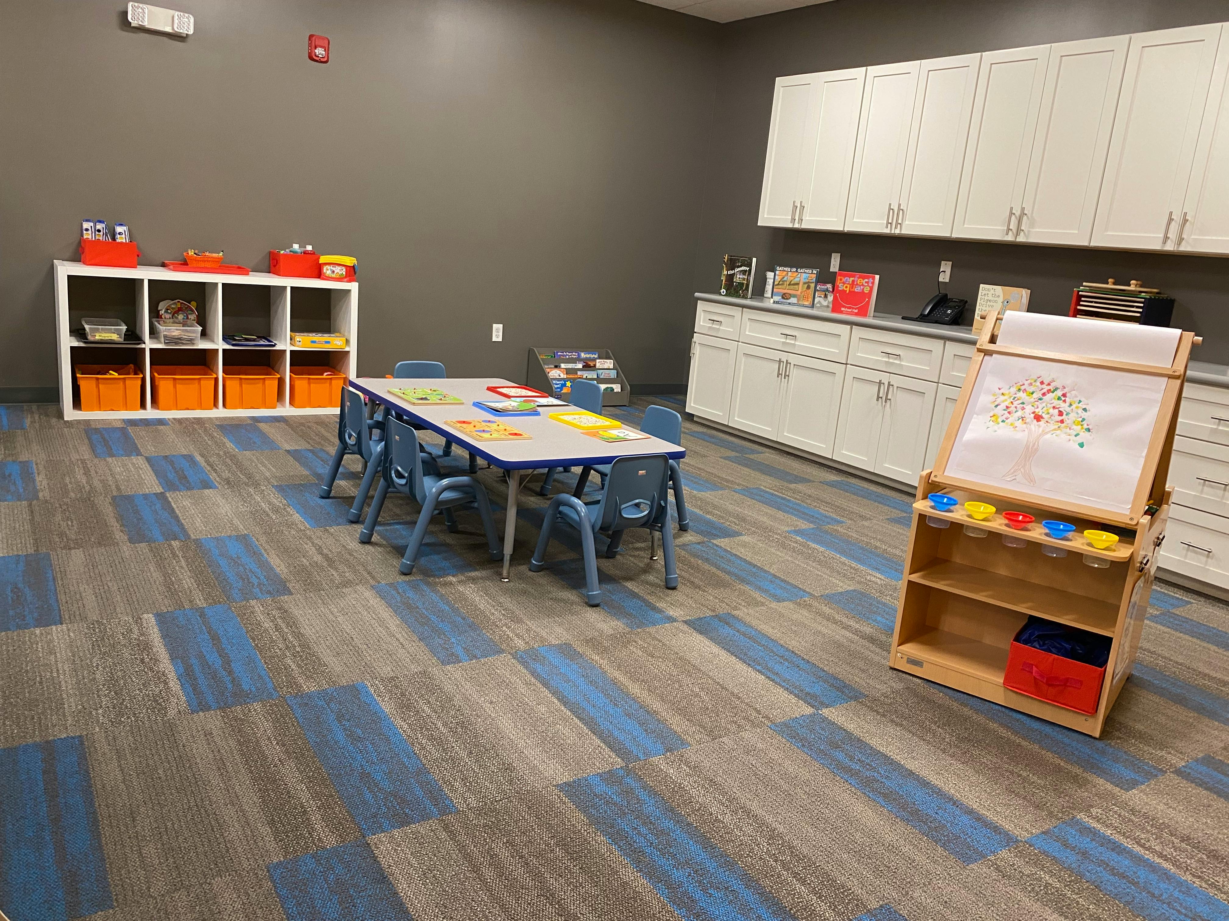 Children's classroom with small table and chairs, storage, and easel