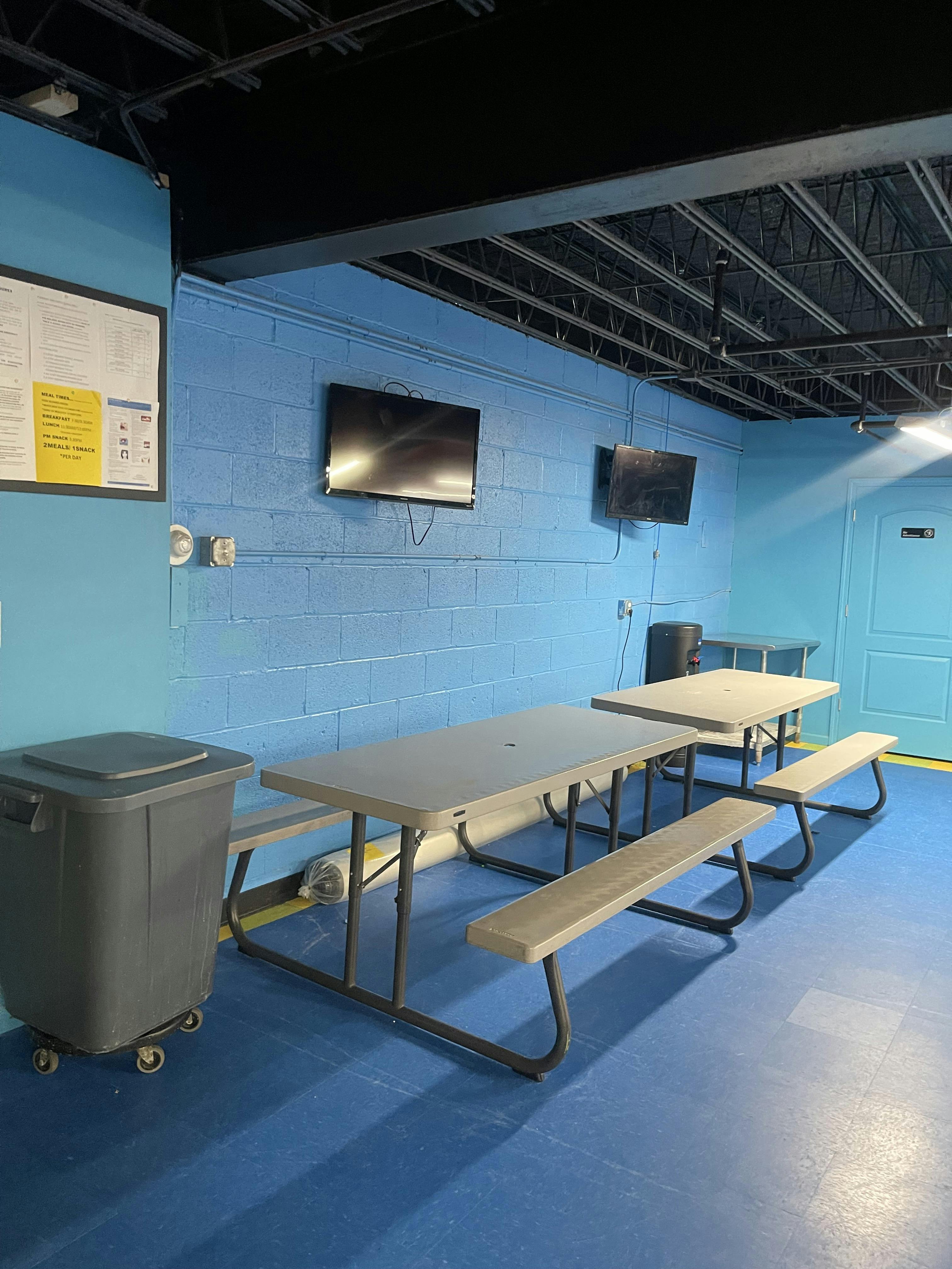 A room with blue walls and floor, two picnic tables, and two wall-mounted TVs