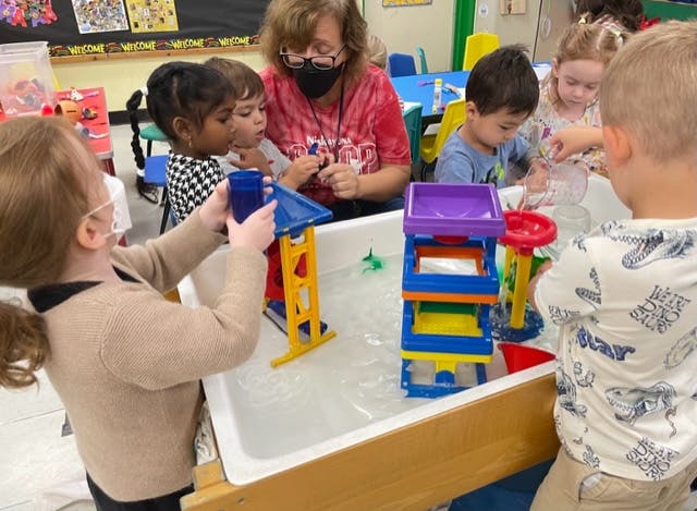 Adult and children playing with water toys in a classroom
