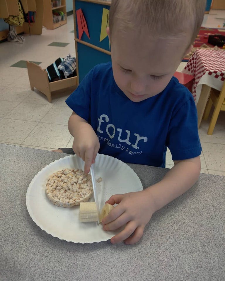 Child cutting a banana on a plate with a rice cake