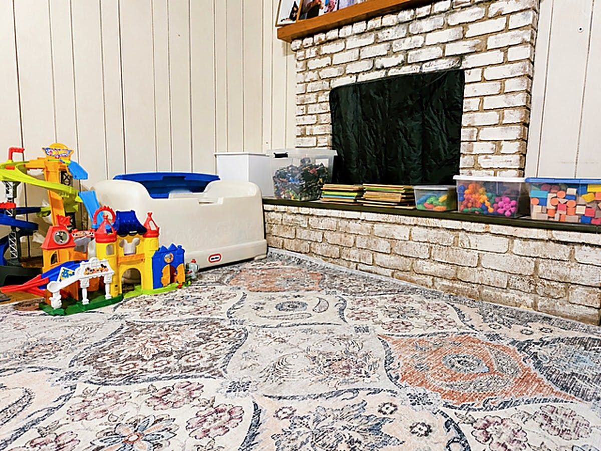 Plastic toy sets and storage bins arranged on a rug in front of a fireplace