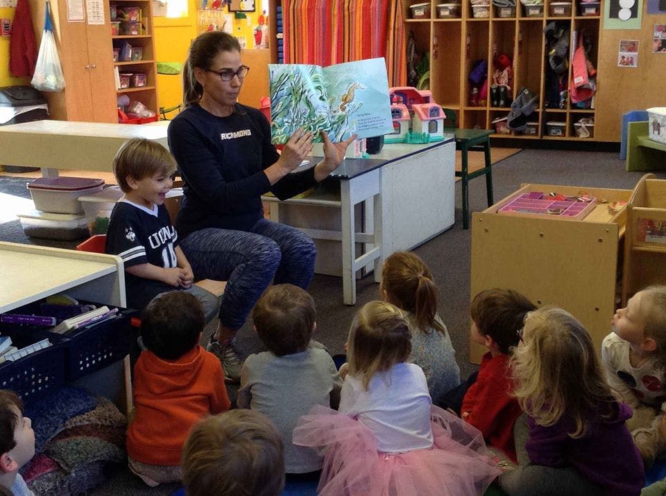 Person reading a book to a group of children in a classroom