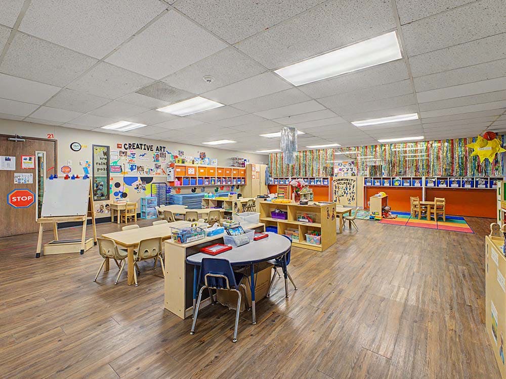 Empty classroom with small tables and chairs, whiteboards, and colorful decorations