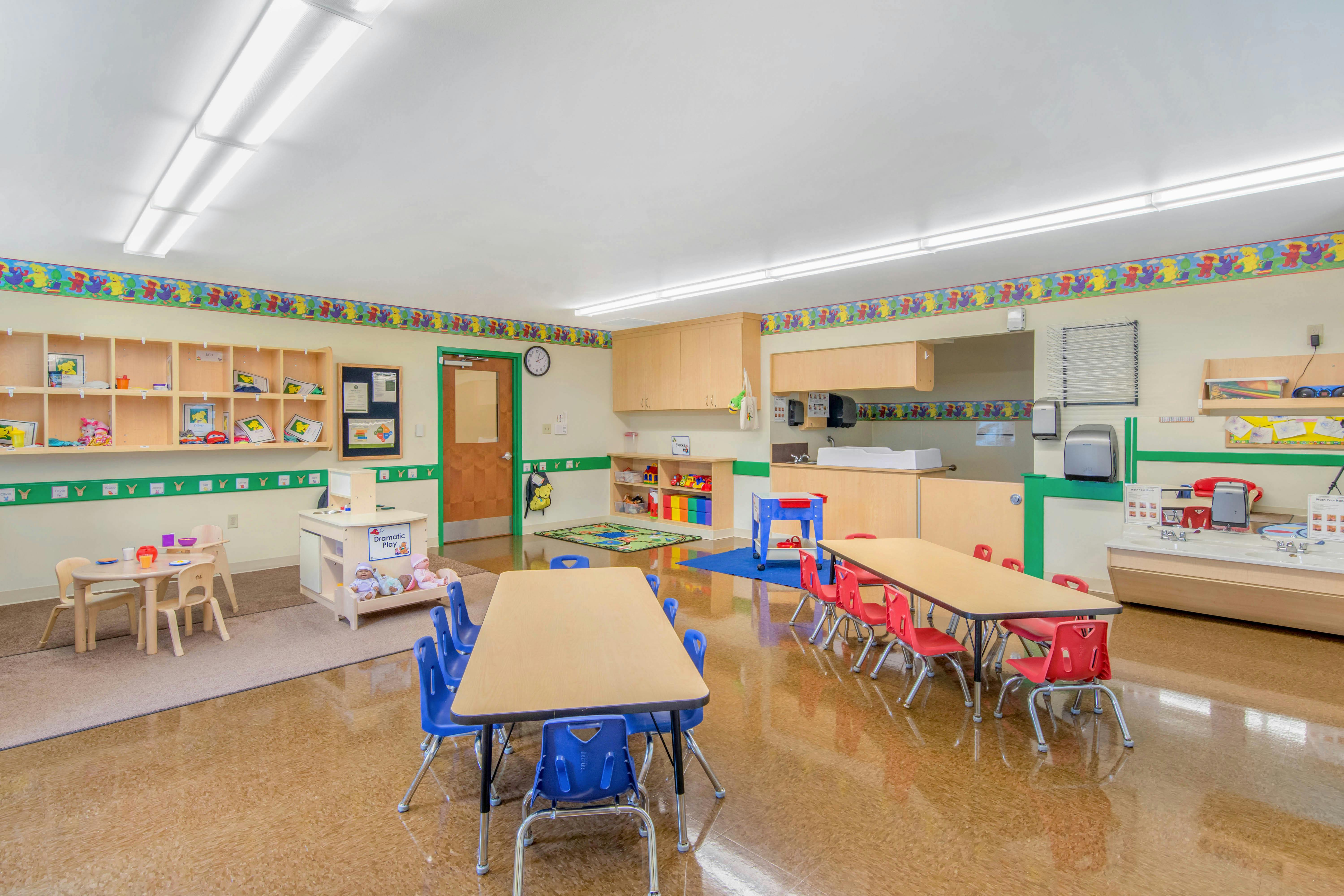 Classroom with child-sized tables and chairs, shelves, and a changing station