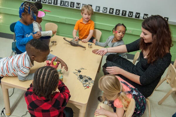 Adult and children gathered around a table in a classroom