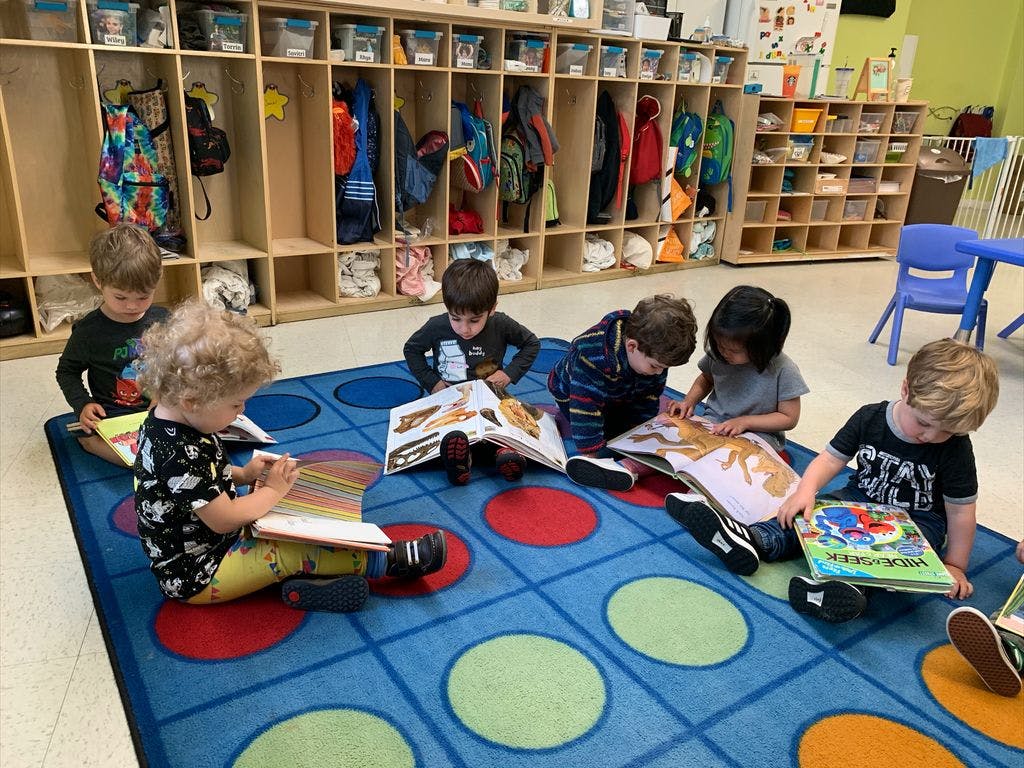 Children sitting on a rug and reading books in a classroom