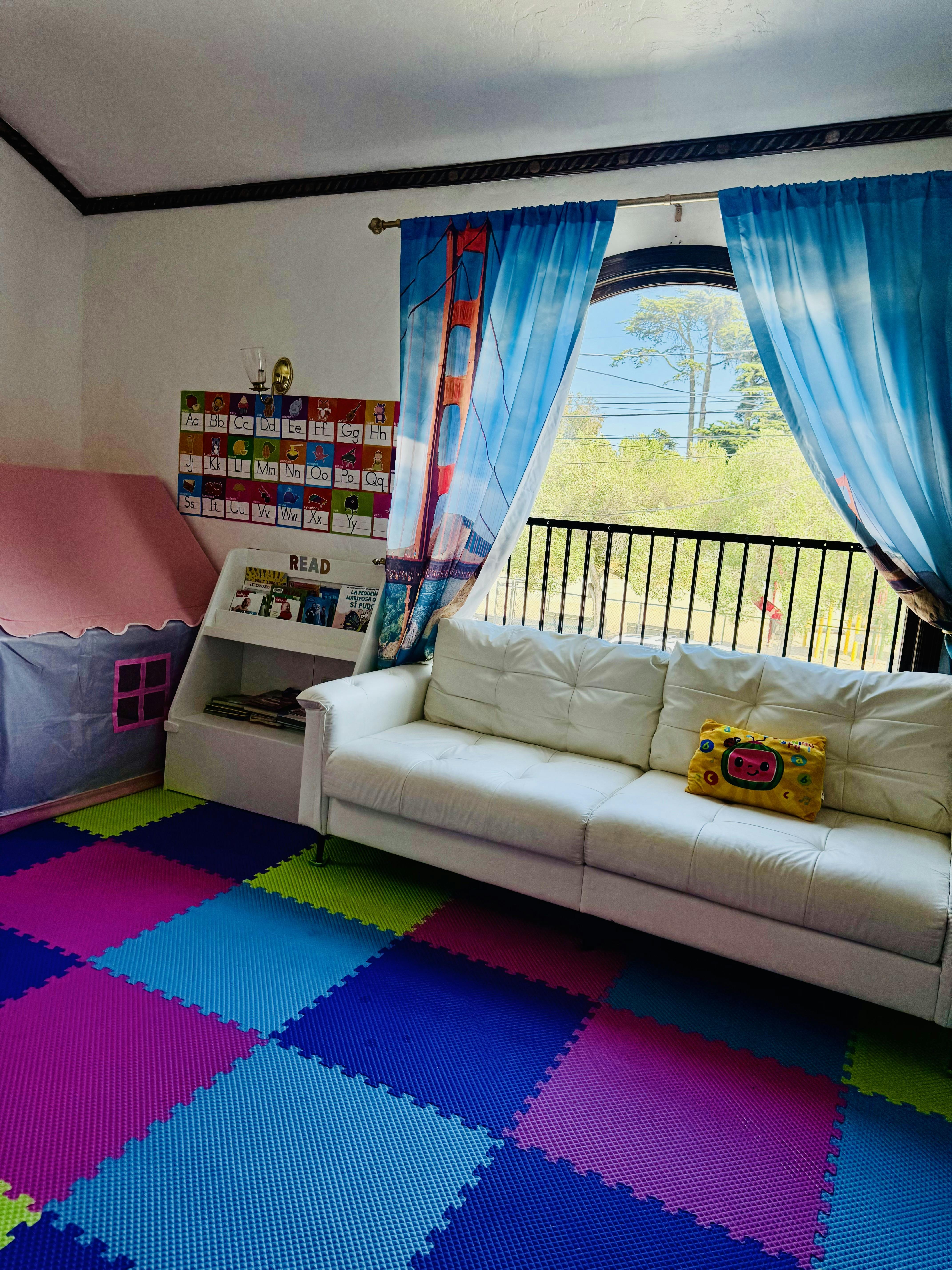 Playroom with colorful floor mats, a white sofa, and a window