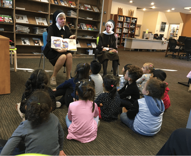 Two people in habits reading to a group of children sitting on the floor