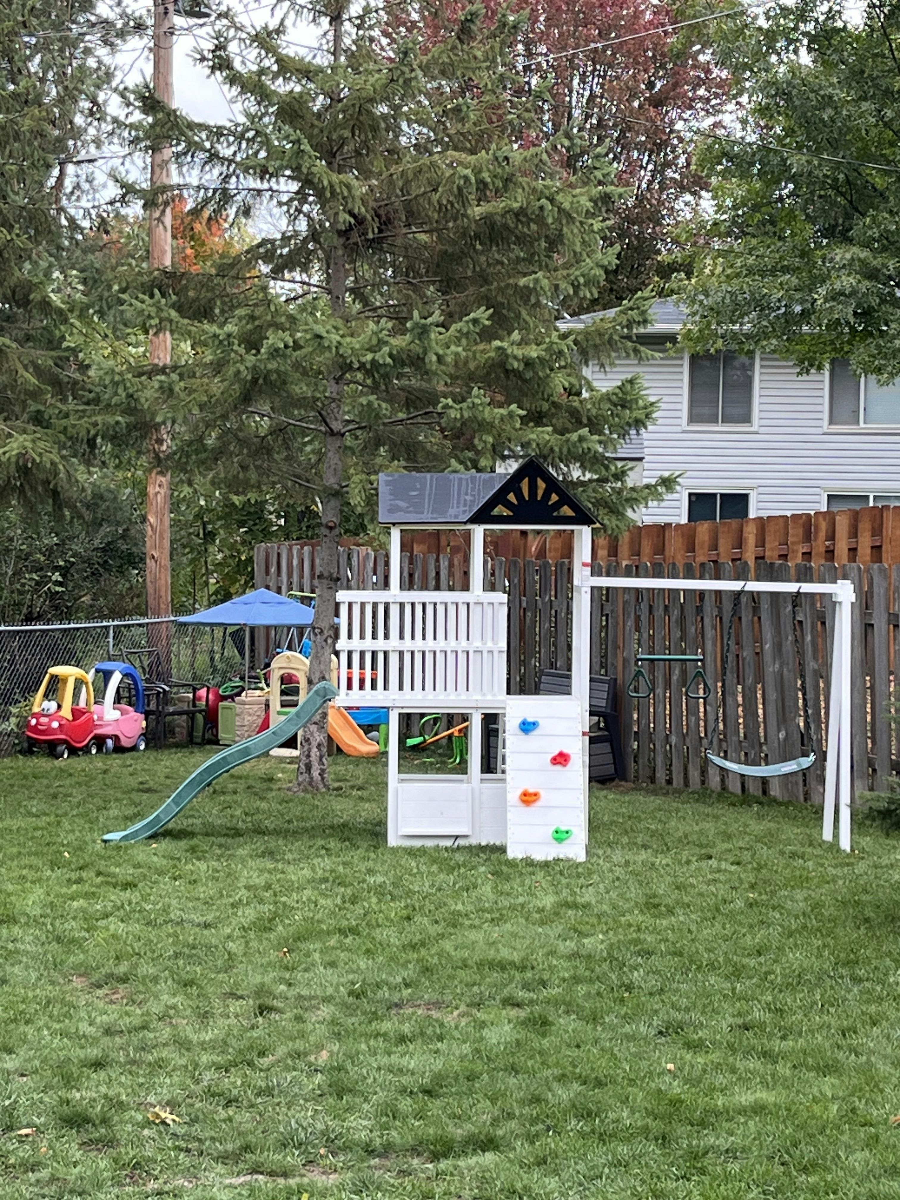 Wooden playset with a slide and climbing wall in a backyard