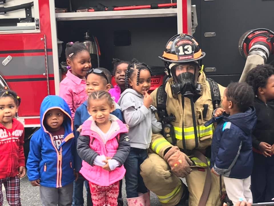 Firefighter in gear kneeling with a group of children in front of a fire truck