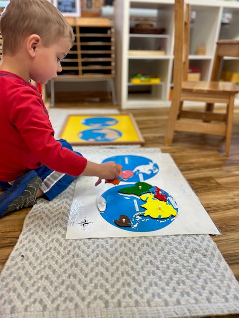 Child playing with a world map puzzle on the floor