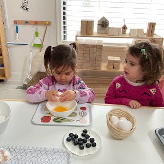 Two children at a table, one cracking an egg into a bowl