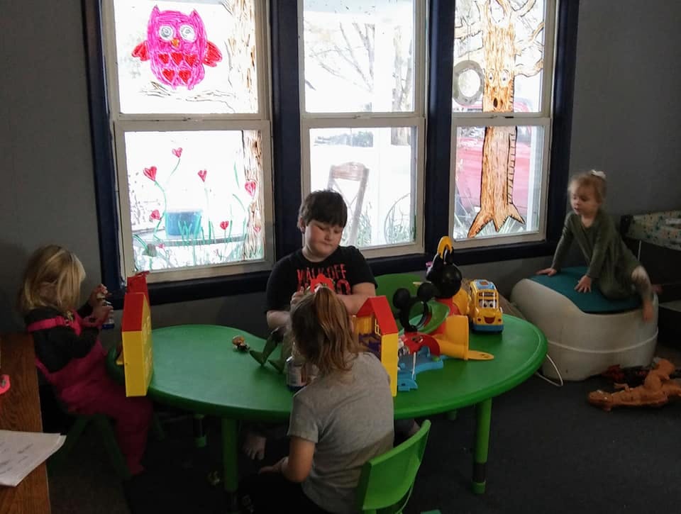 Three children playing at a green table, one child on a beanbag chair