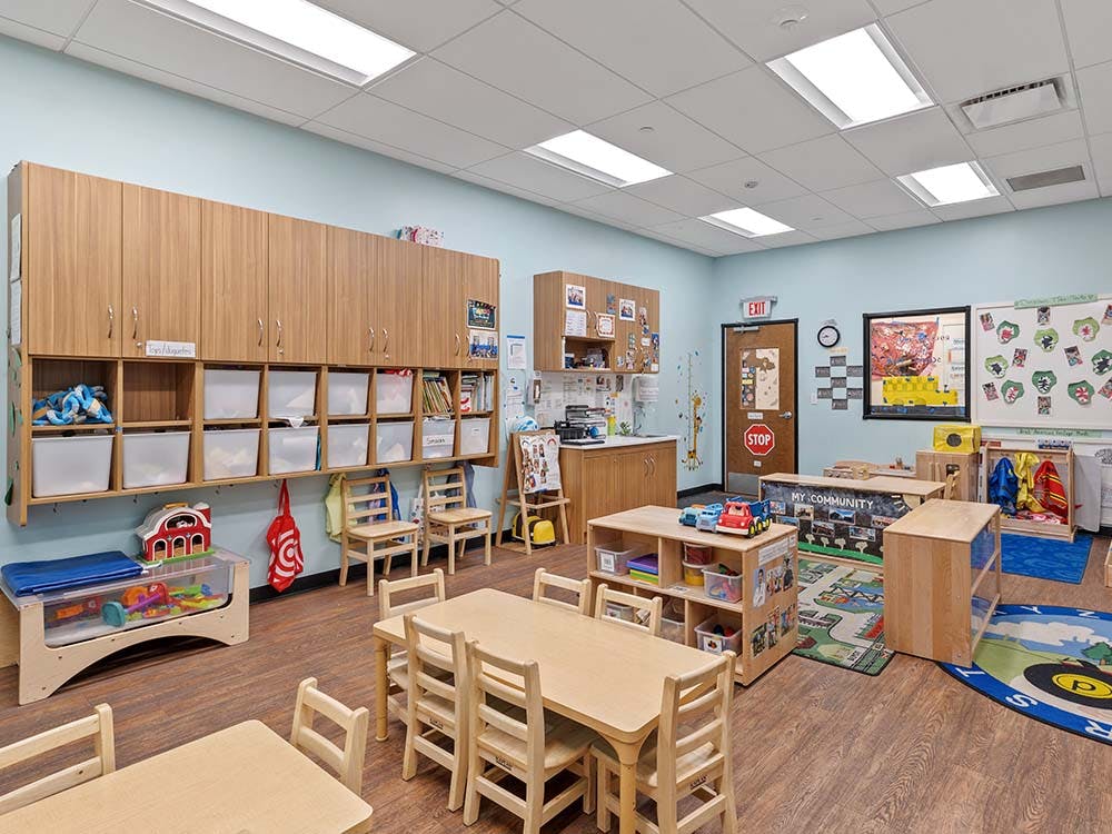 Classroom with small wooden tables and chairs, storage cabinets, and play areas
