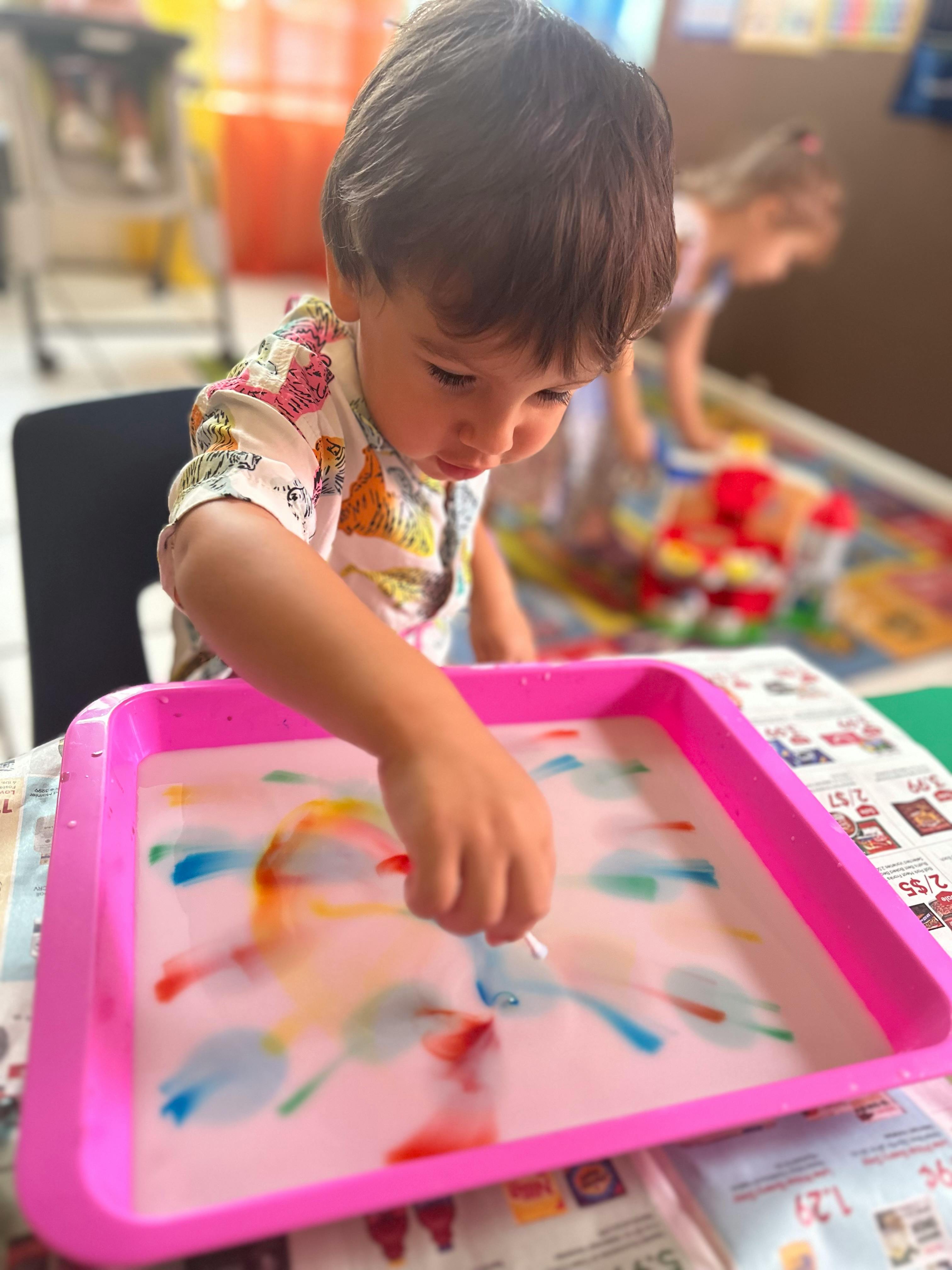 Child playing with colorful liquid in a pink tray