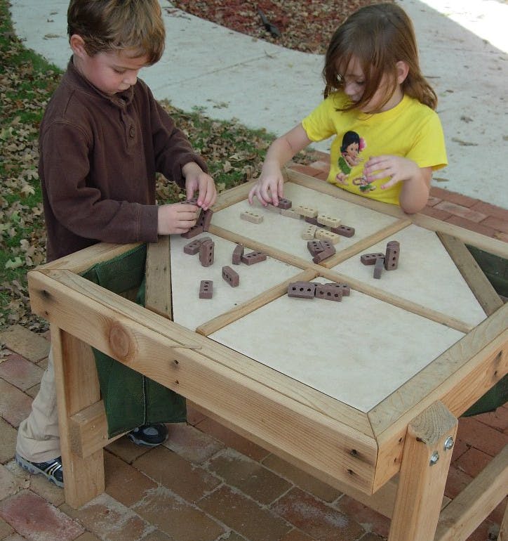 Two children playing with small blocks on a wooden table