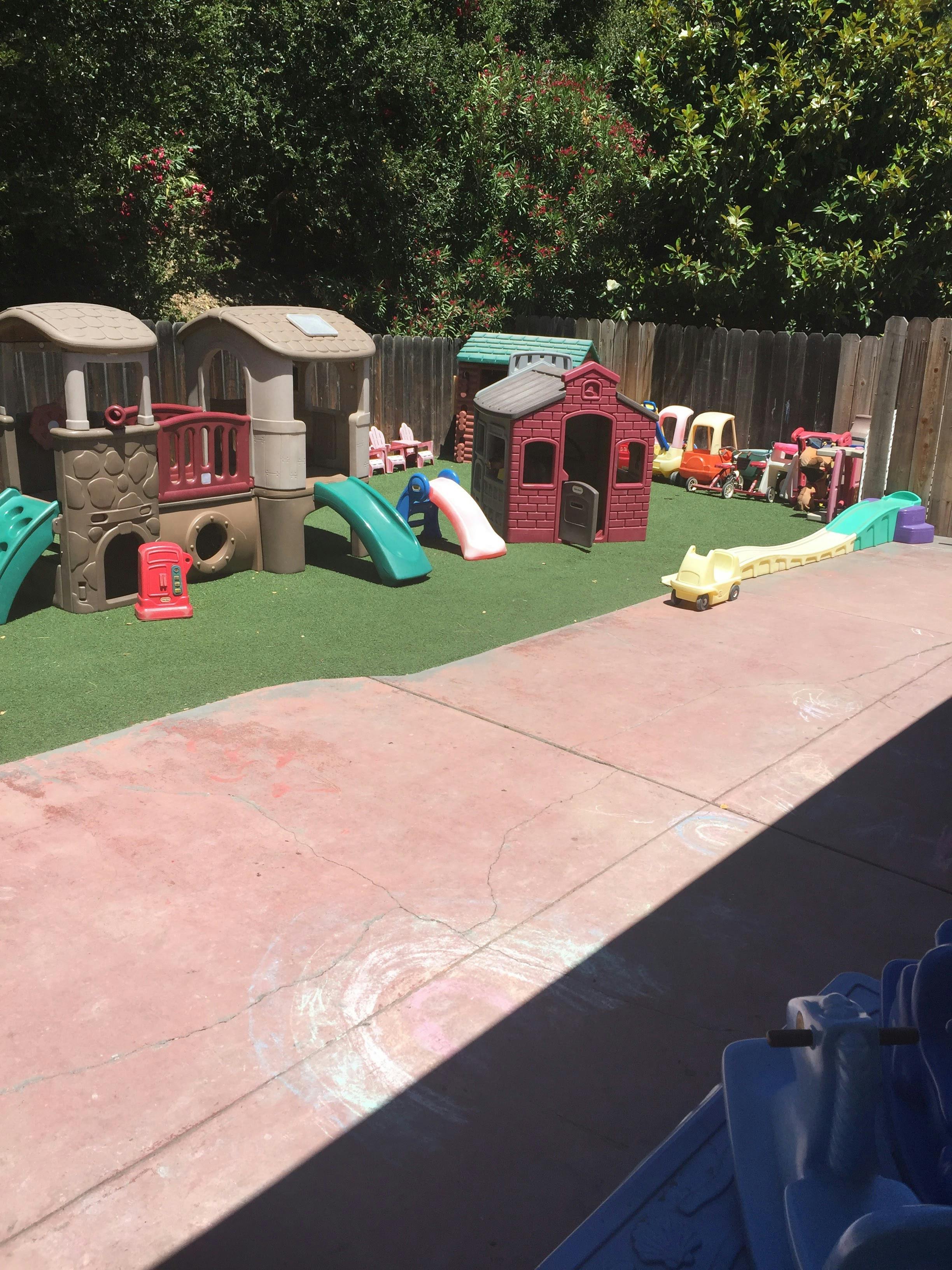Outdoor playground with slides, playhouses, and ride-on toys on artificial turf