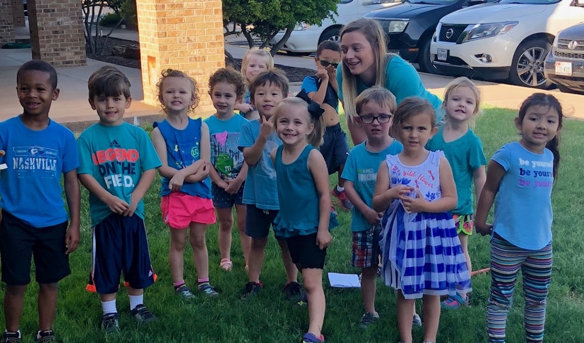 Adult and group of children standing on grass