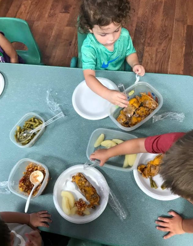 Child serving food from containers onto a plate at a table