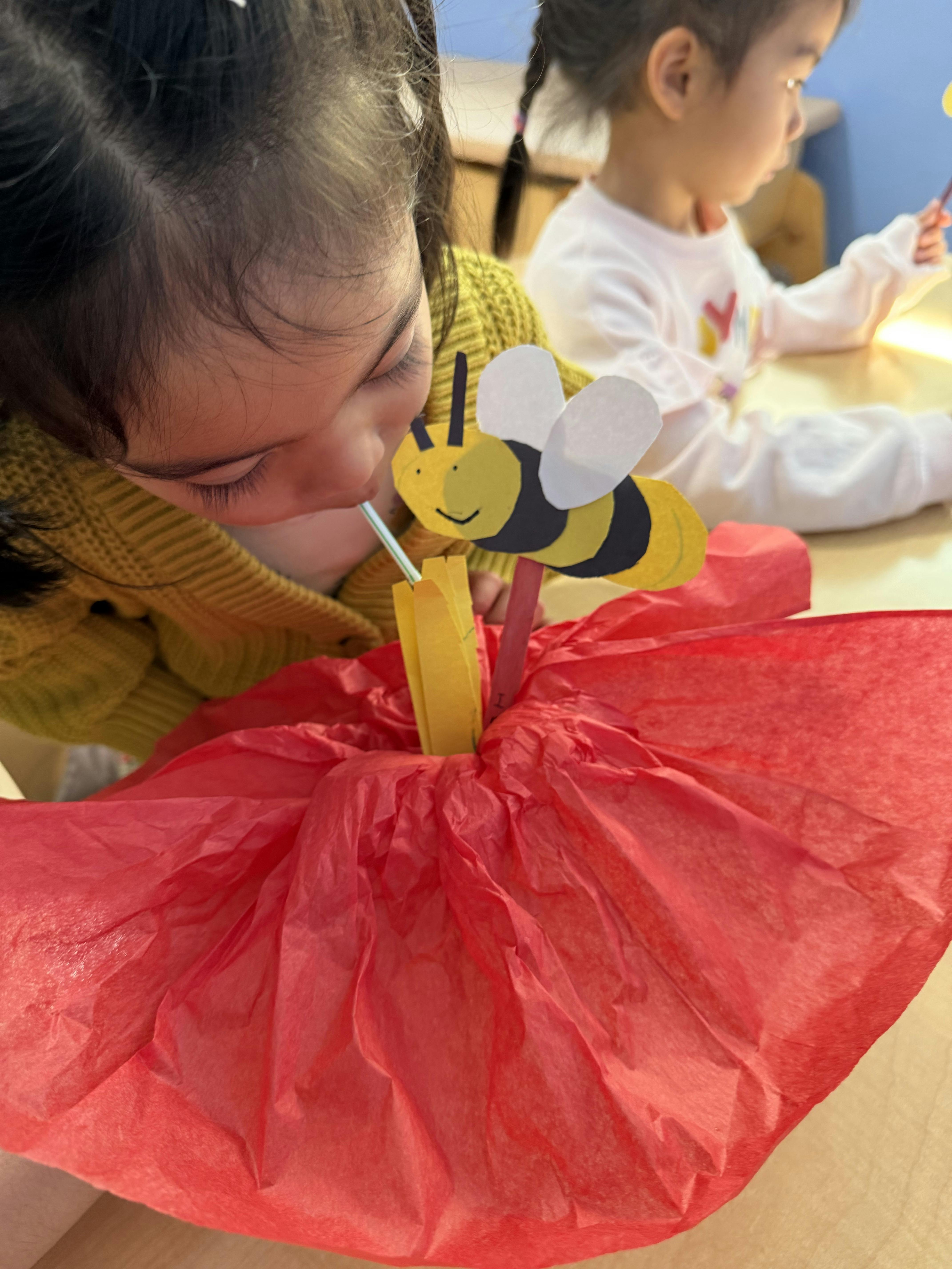 Child blowing through a straw at a paper bee and flower craft