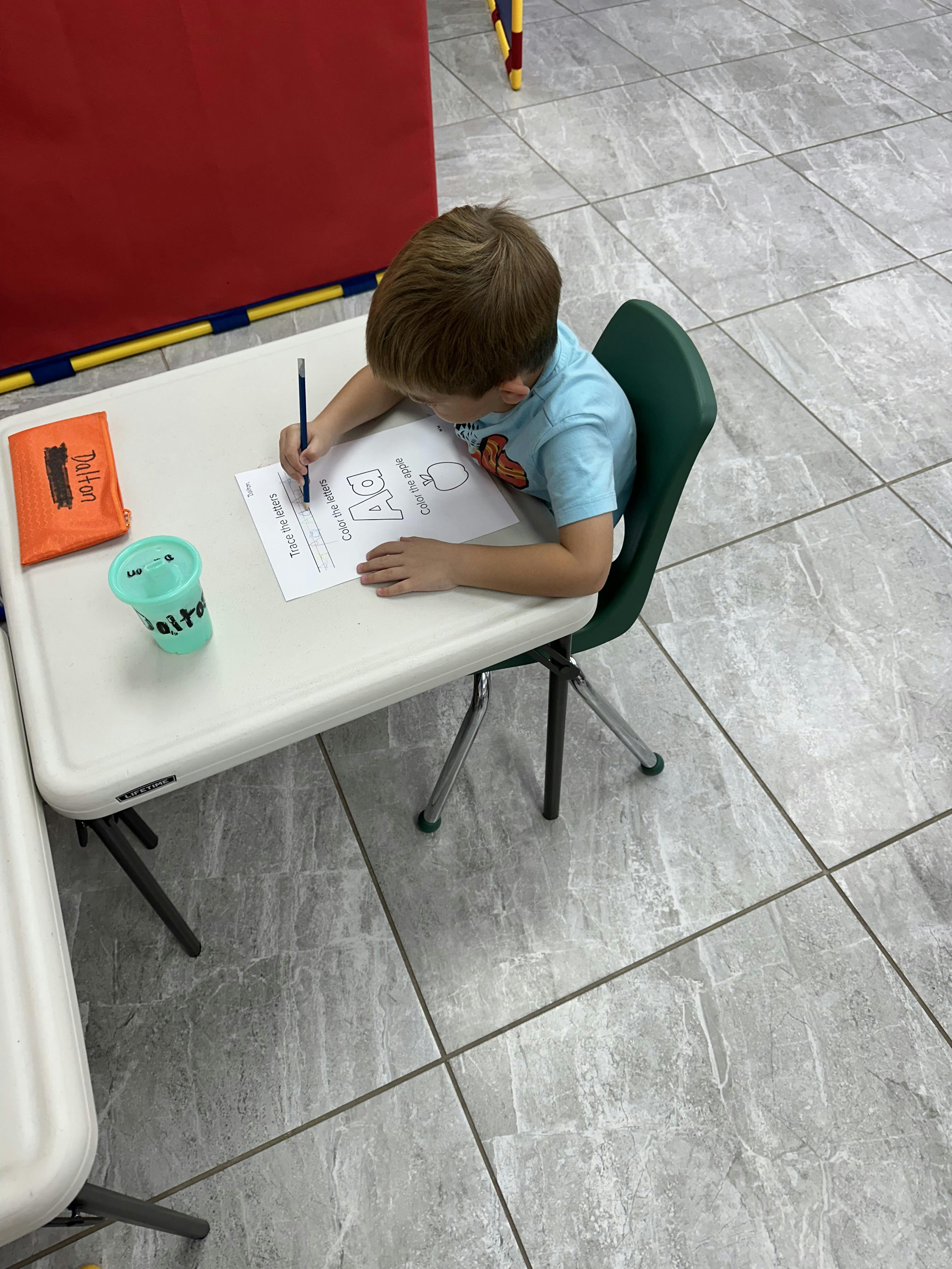 Child sitting at a table writing on paper with a pencil