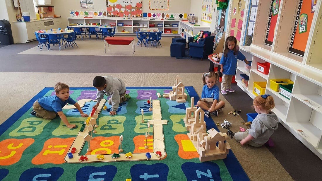 Children playing with blocks and toys on a colorful rug in a classroom