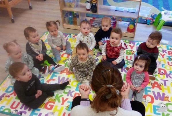 Many babies and a person sitting on a colorful alphabet mat in a classroom