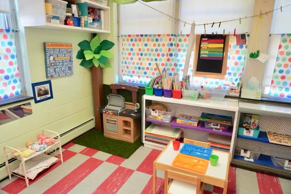 Classroom with play kitchen, shelves, and small table with chairs