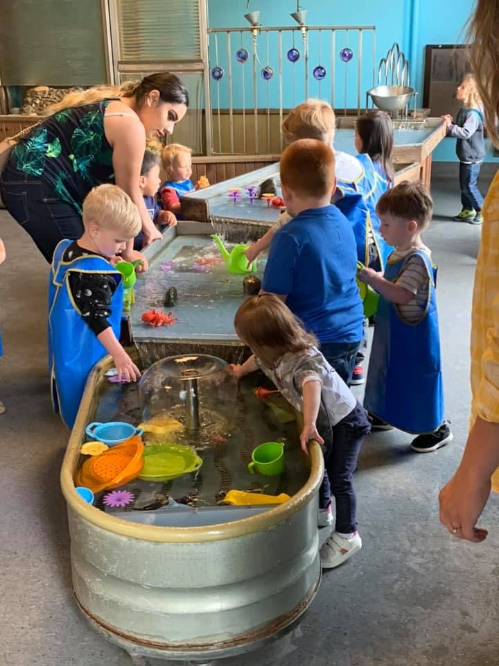 Adult and children playing with water and toys at a water table