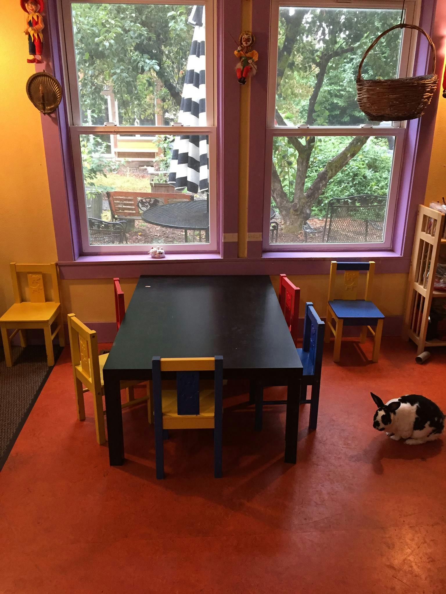 Black and white rabbit on a red floor next to a table and chairs