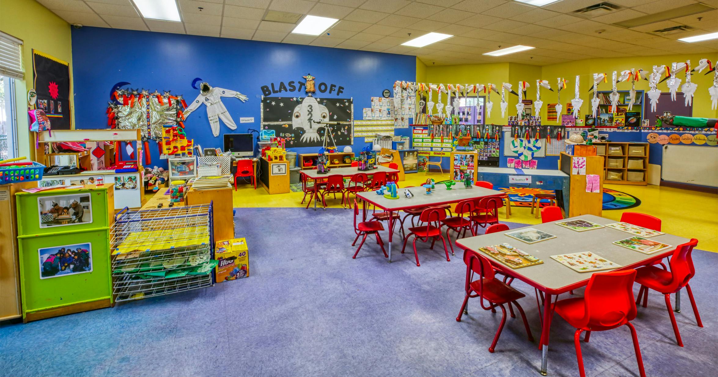 Classroom with small tables and chairs, space-themed decorations, and a "BLAST OFF" sign