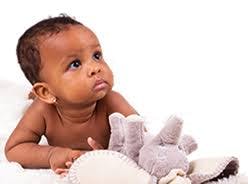 Baby looking up while lying on stomach next to a stuffed animal