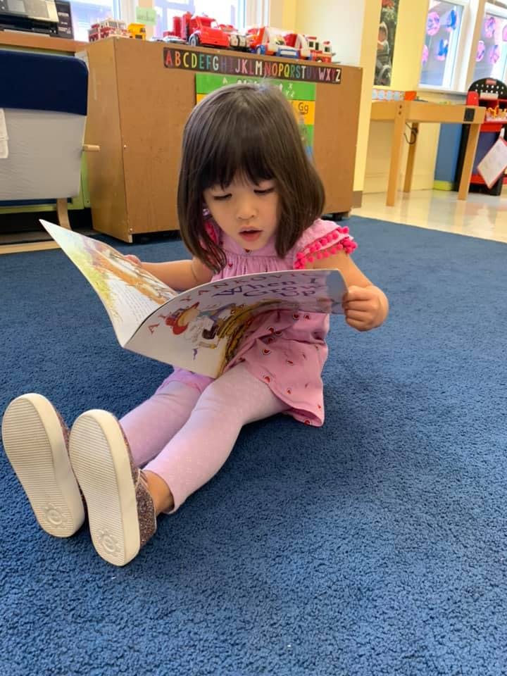 Child sitting on floor reading a book in a classroom