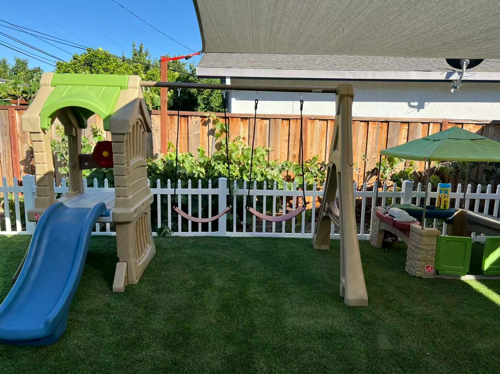 Child's playset with a slide and swings on artificial grass in a backyard