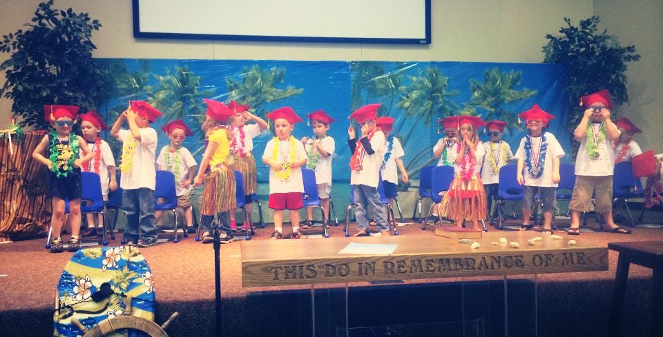 Children in red hats and leis on a stage