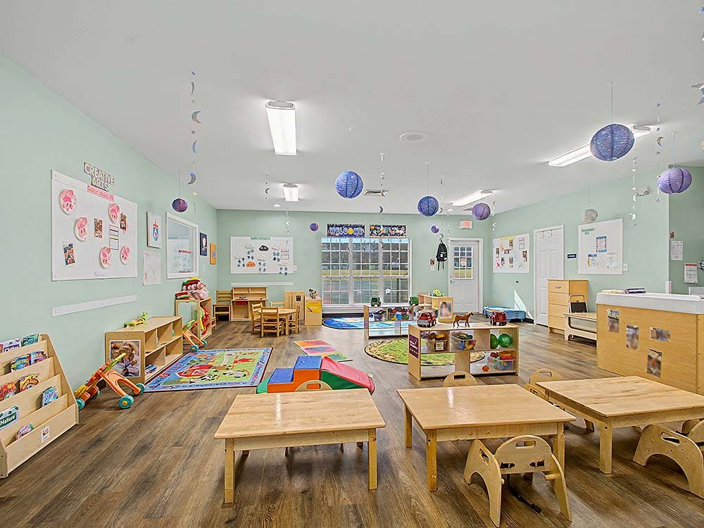 Classroom with small tables and chairs, shelves with toys, and wall decorations