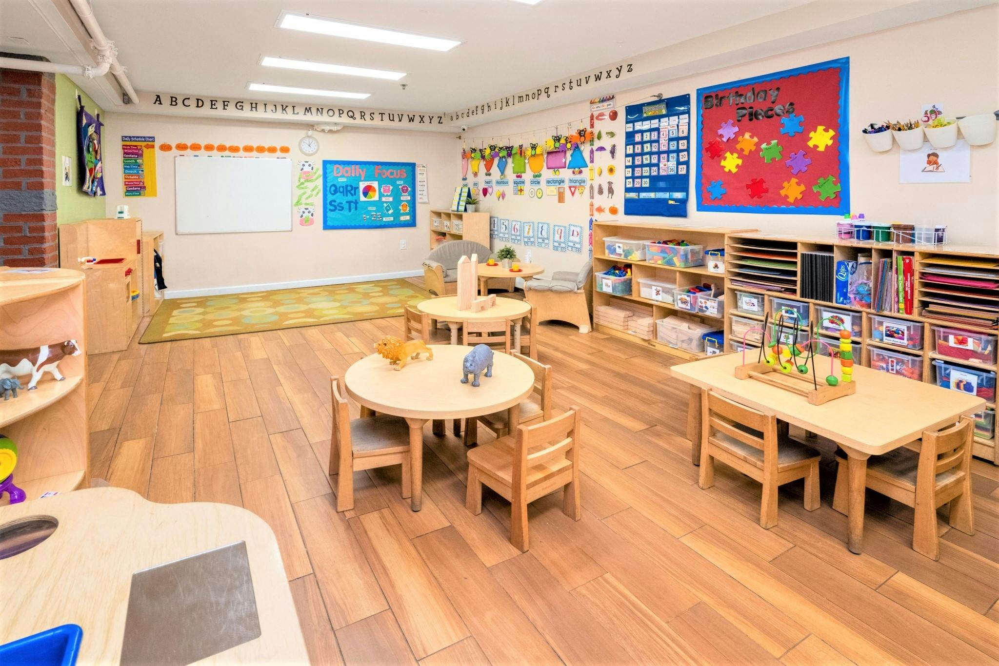 Classroom with small tables and chairs, shelves with toys and books, and colorful decorations