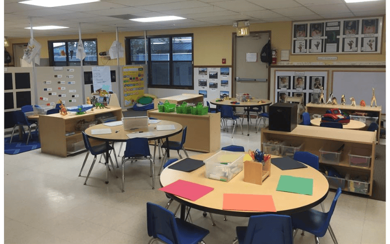 Classroom with multiple round tables and chairs, shelves, and decorations