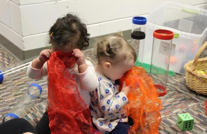 Two children playing with colorful fabric on the floor