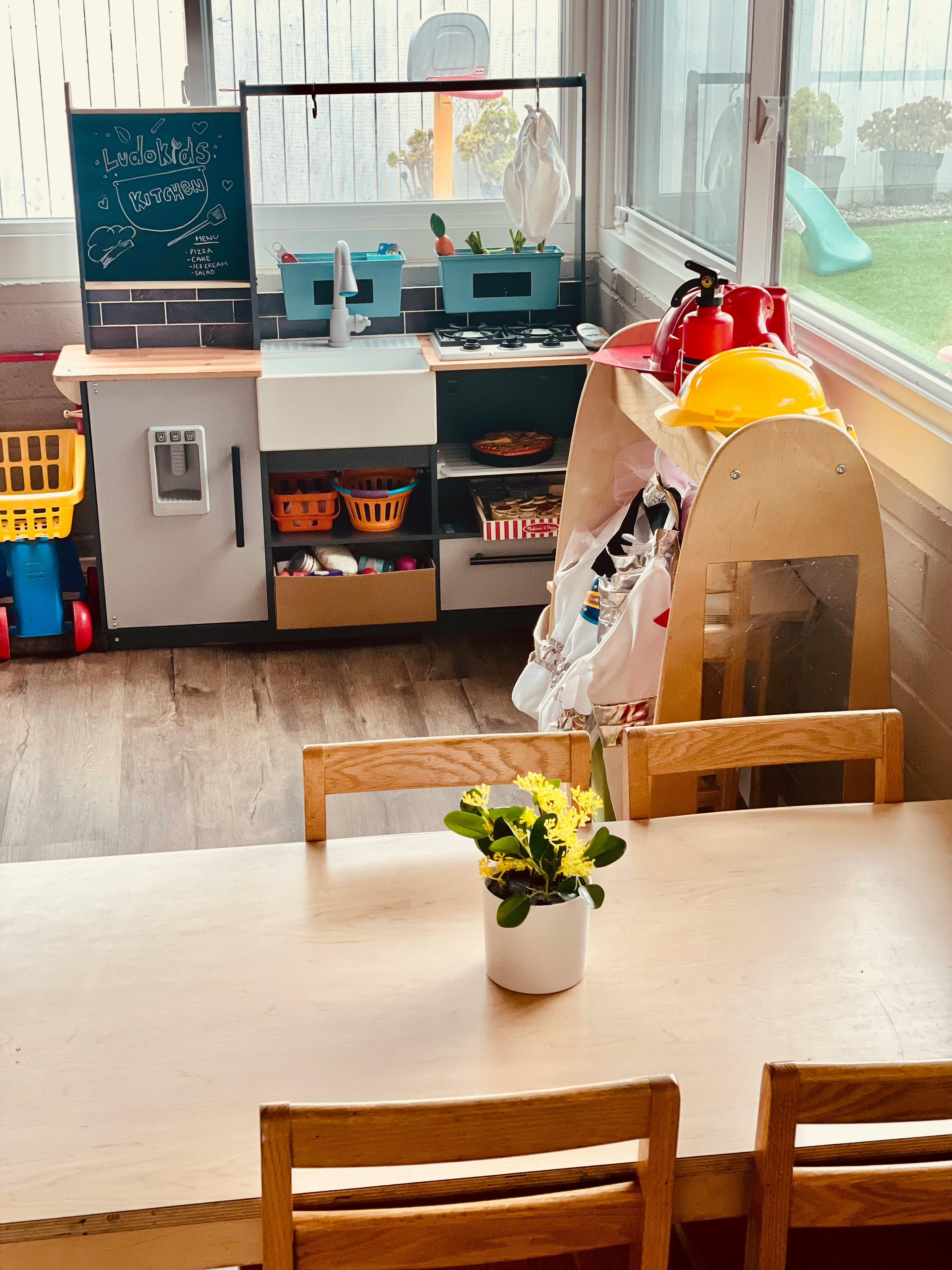 Play kitchen with a chalkboard, sink, and stove next to a table with chairs