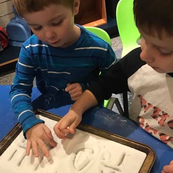 Two children writing in sand on a tray