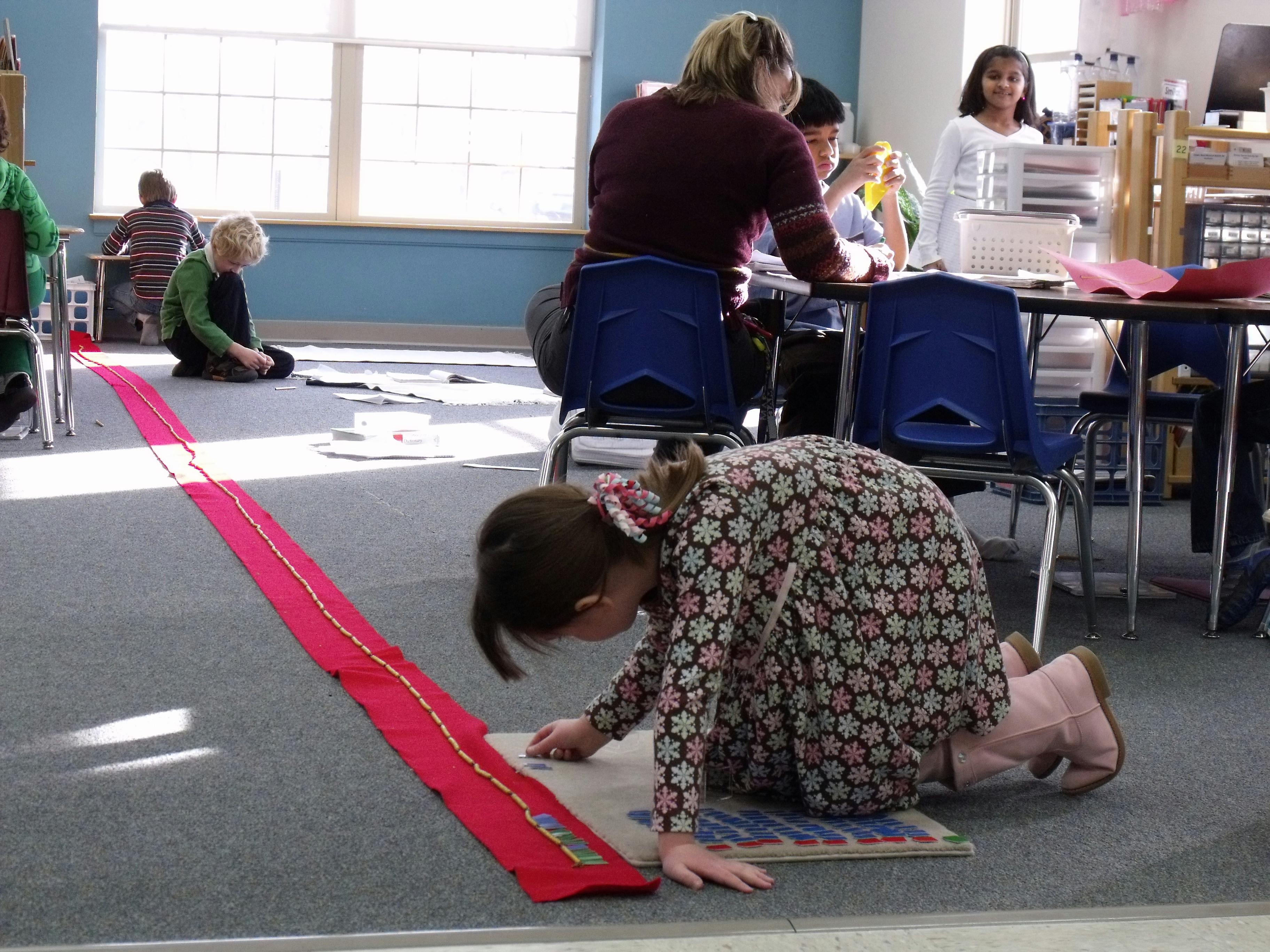 Child kneeling on floor looking at a book with a long red fabric strip next to them
