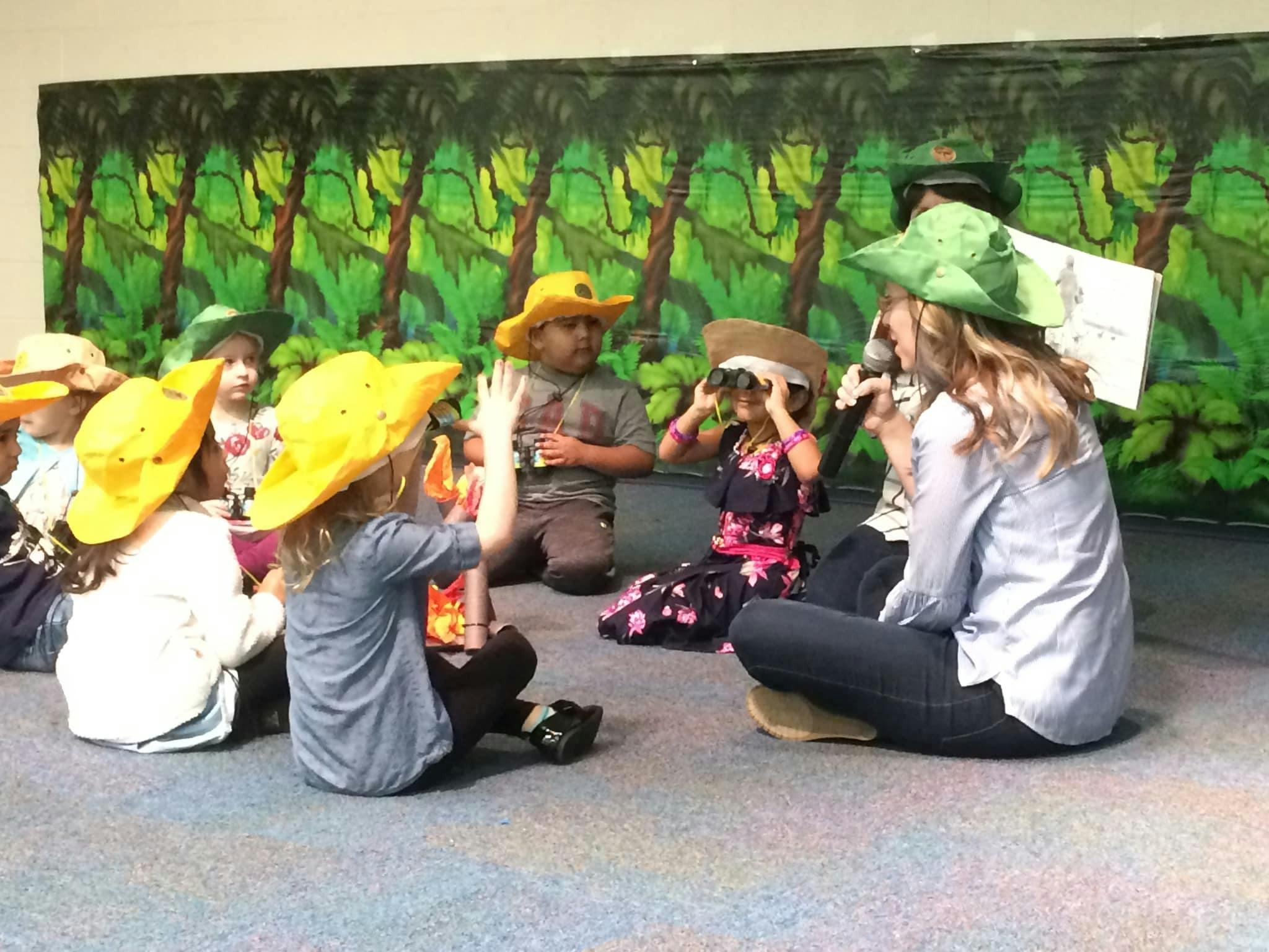 Adult and children in hats sitting on floor, adult reading to children