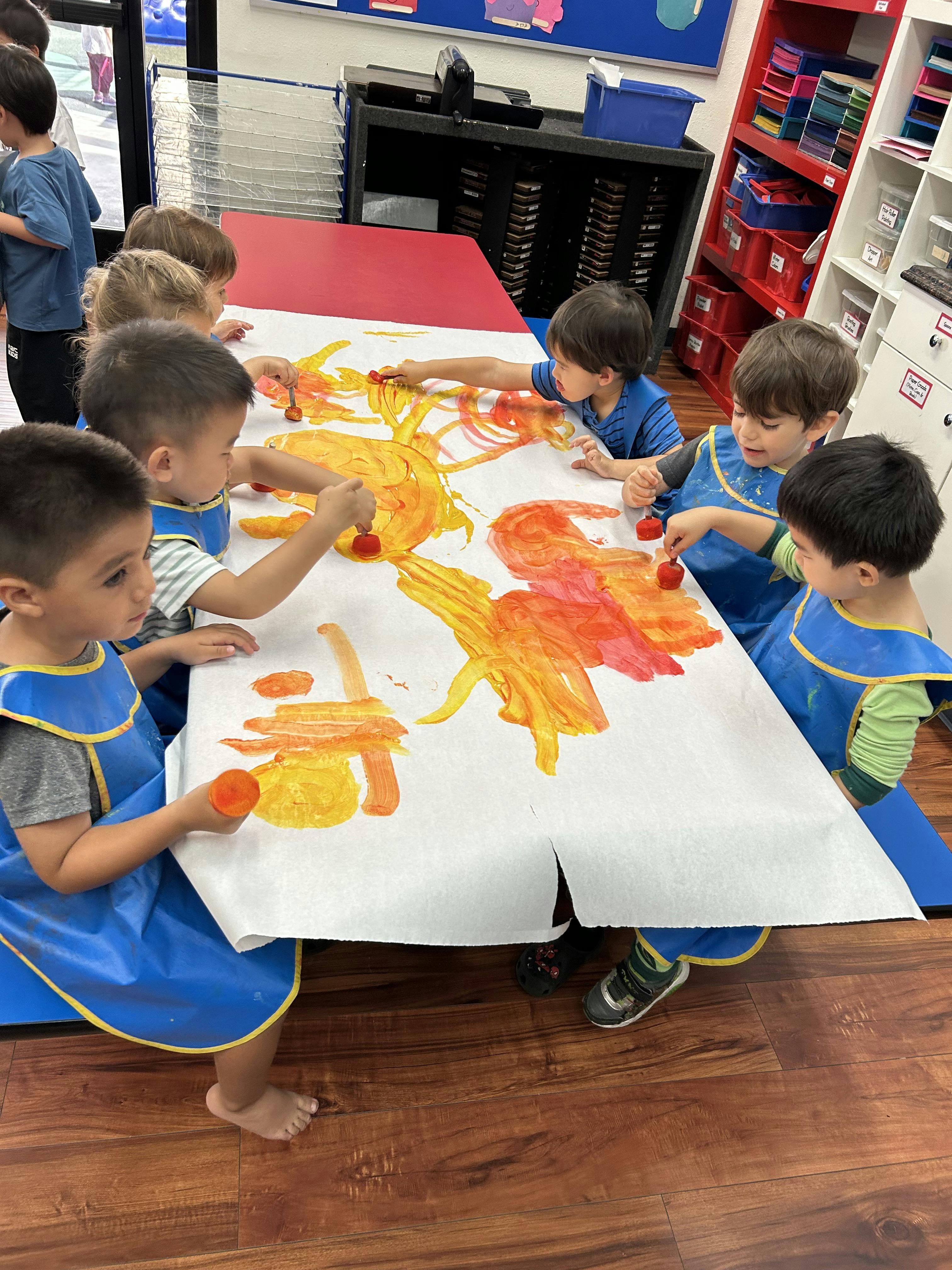 Group of children wearing blue aprons painting with sponges on a large paper