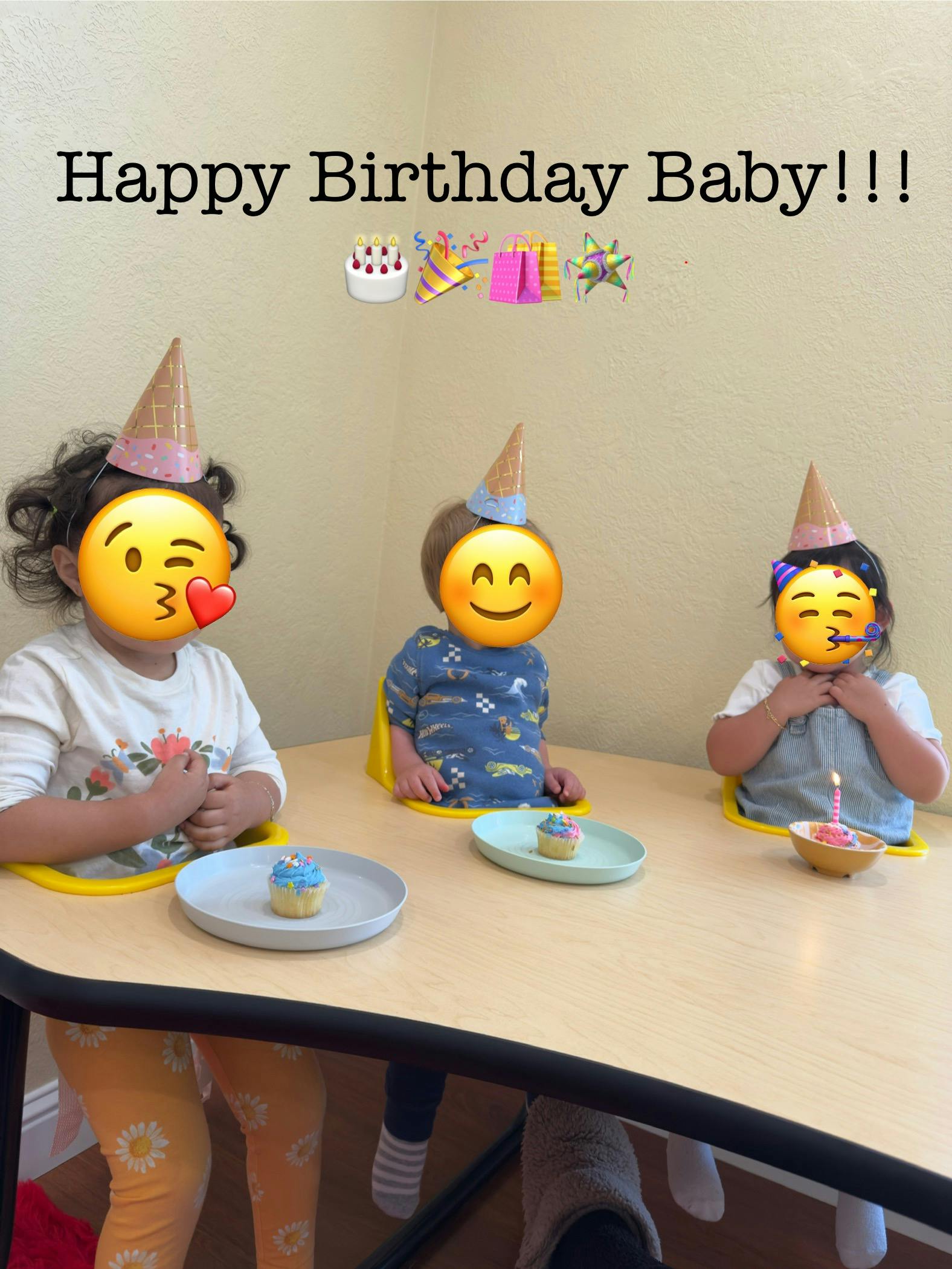 Three children wearing party hats sitting at a table with cupcakes