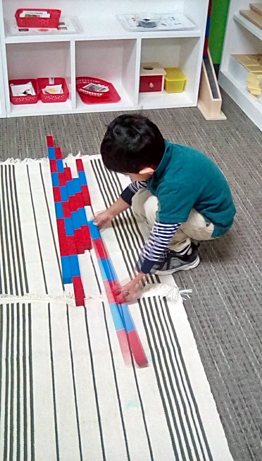 Child crouching on a striped rug, arranging red and blue blocks