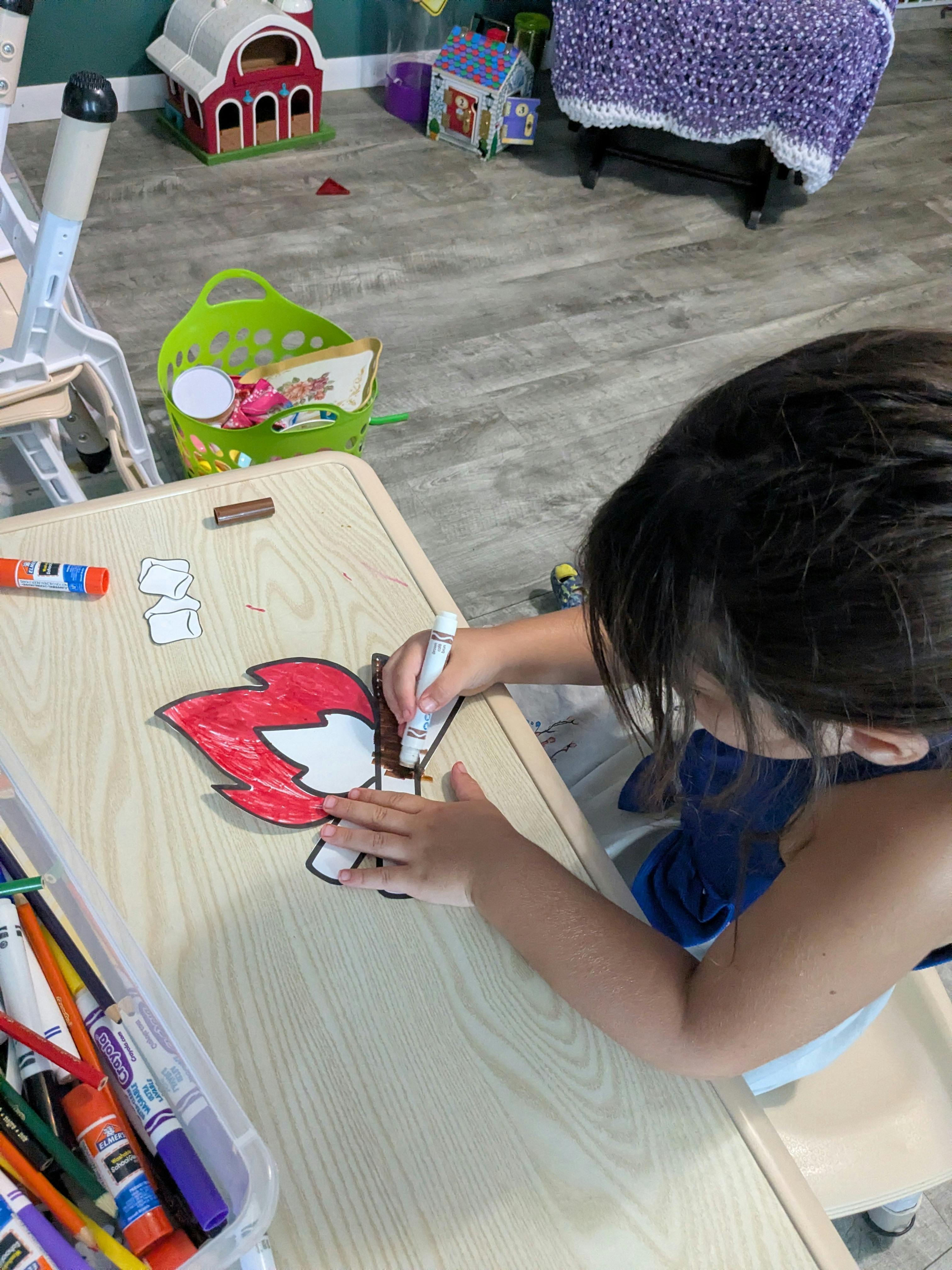 Child coloring a paper campfire craft at a table